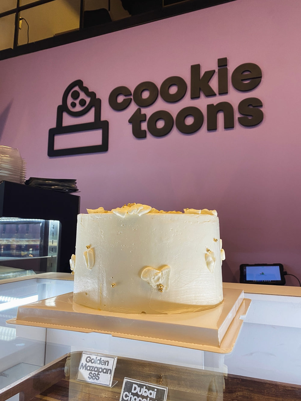 Pastel blanco con flores y acentos dorados en la tienda Cookie Toons